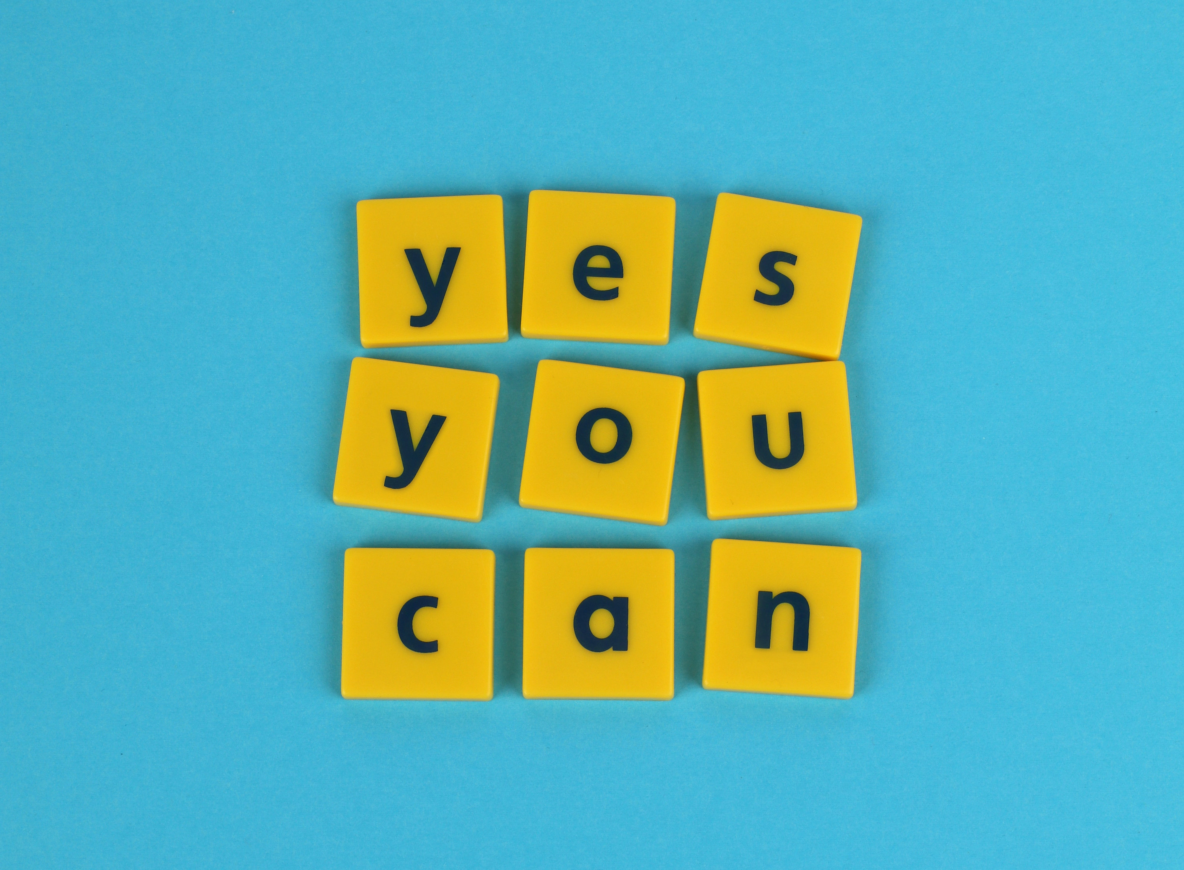 Gelbe Dominosteine auf blauem Hintergrund mit dem Schriftzug "Yes you can" 