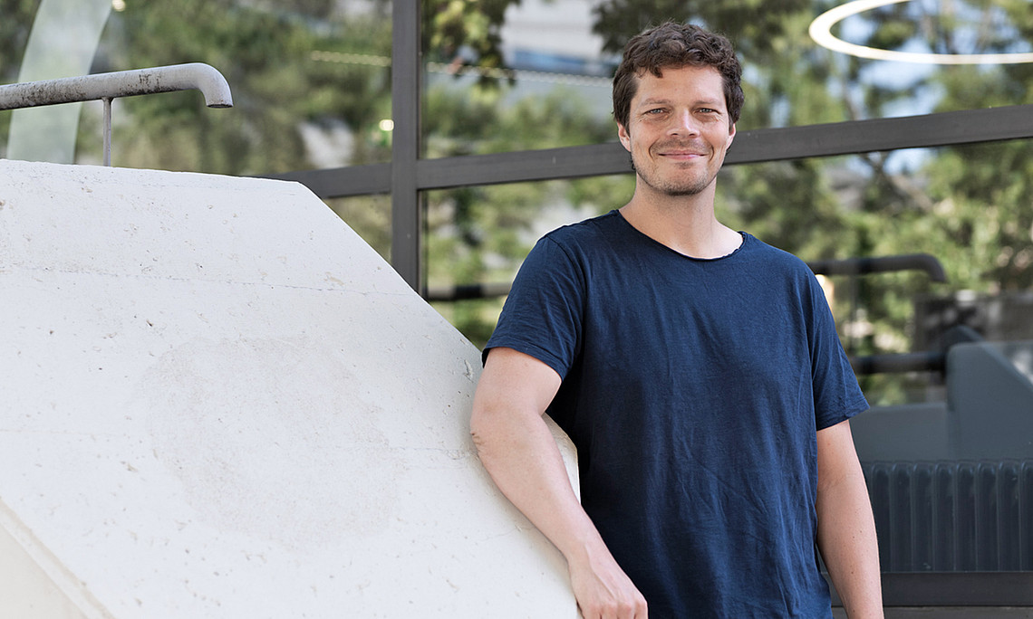 David Clases vor dem Mensa Space der Uni Graz an ein breites Beton-Stiegengeländer gelehnt