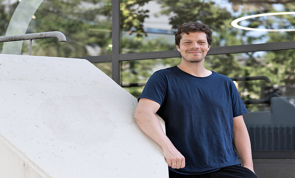 David Clases vor dem Mensa Space der Uni Graz an ein breites Beton-Stiegengeländer gelehnt