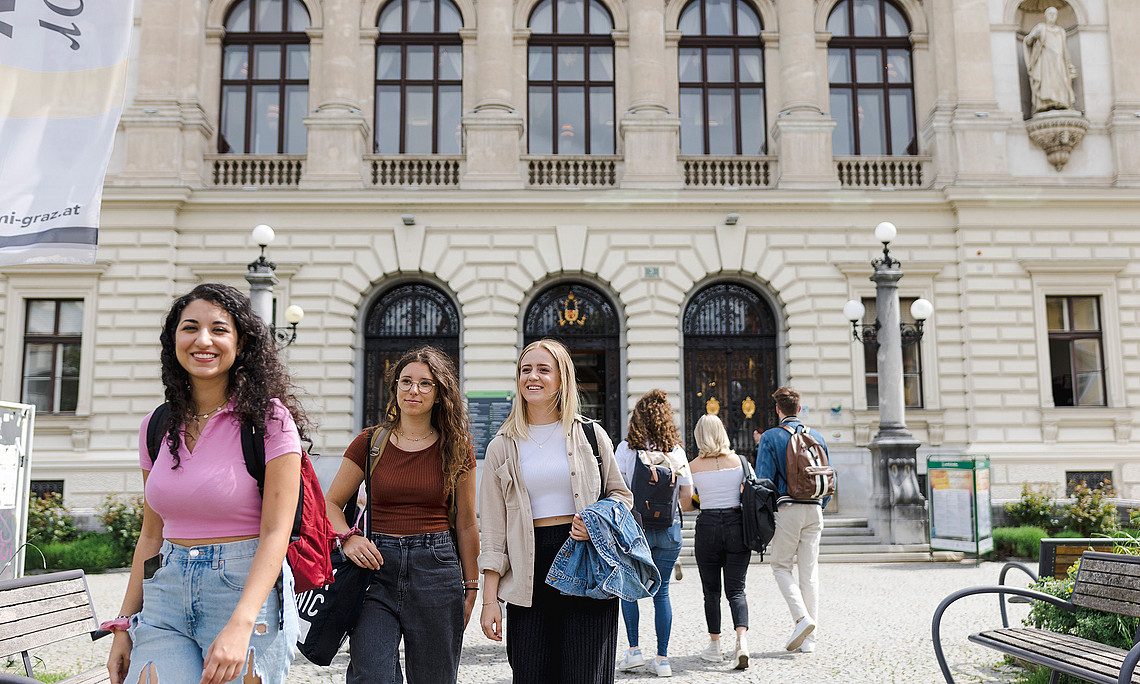 Eine Gruppe von drei jungen Frauen steht vor einem historischen Gebäude.