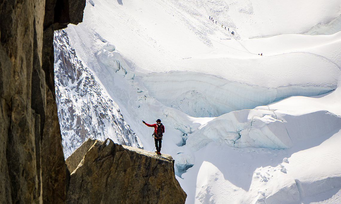 Wanderer auf Felswand mit Ausblick auf Gletscher: Mut zur Veränderung heißt Mut zum Leben