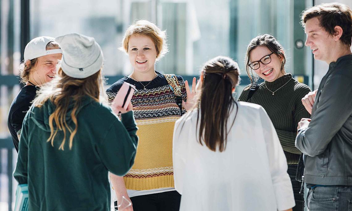 eine Gruppe mit fünf sechs jüngeren Frauen und Männern steht in einem Kreis und spricht