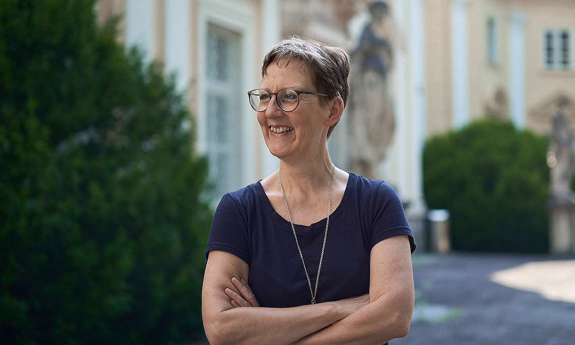 Musikwissenschaftlerin Susanne Kogler mit verschränkten Armen und Blilck nach links im Garten des Meerscheinschlössls