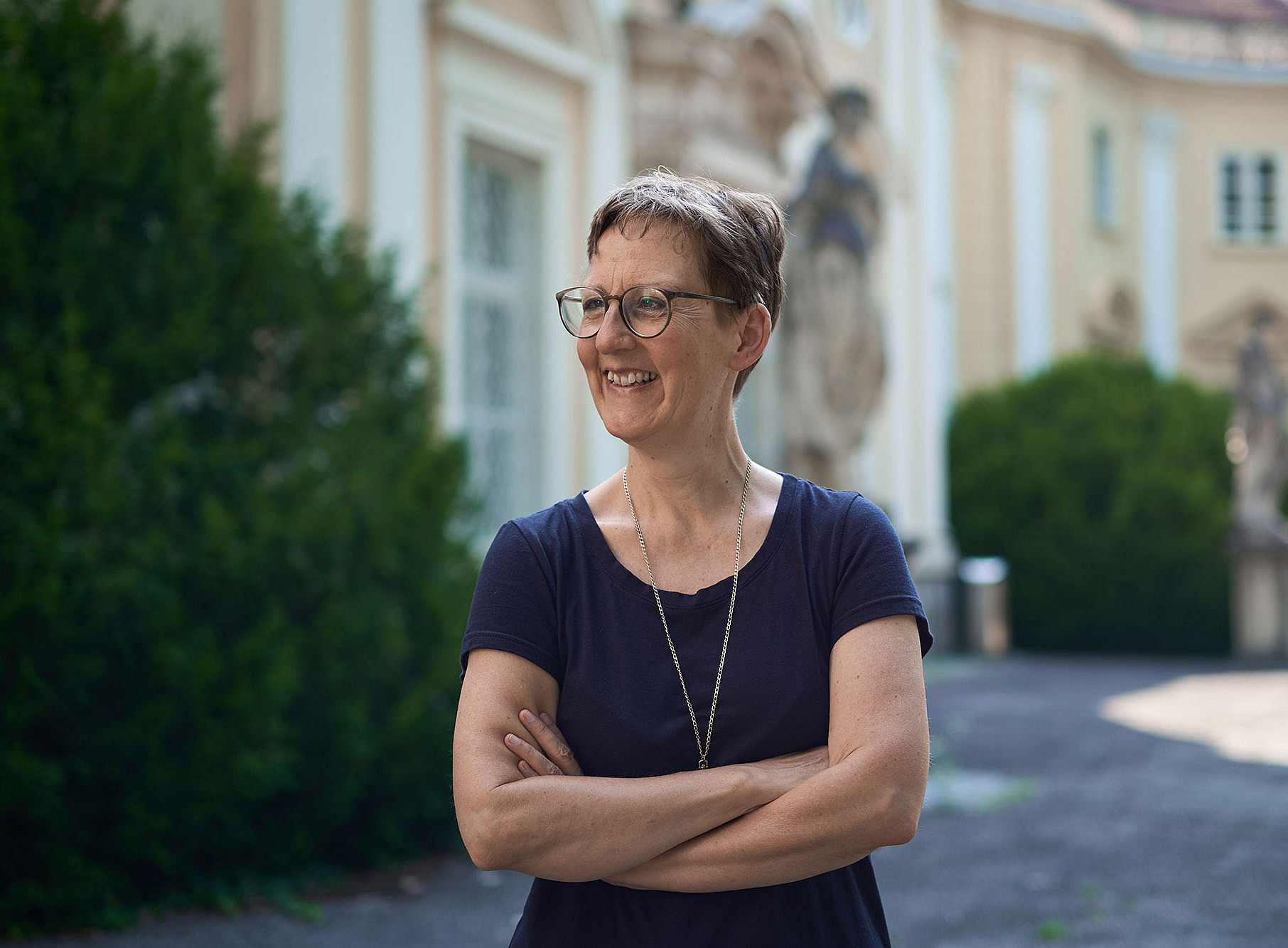 Musikwissenschaftlerin Susanne Kogler mit verschränkten Armen und Blilck nach links im Garten des Meerscheinschlössls ©Joel Kernasenko