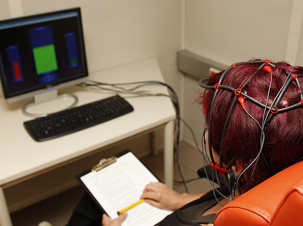 Eine Person mit aufgesetzter EEG Kappe sitzt vor einem Monitor und übt Neurofeedback ©Uni Graz/Tzivanopoulos