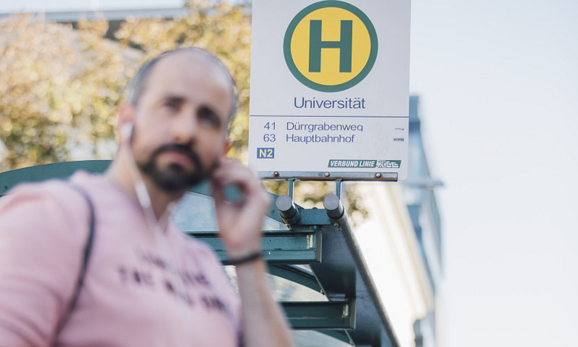 Vereinbarkeit von Studium und Lehrtätigkeit - Person vor Bushaltestelle der Uni Graz