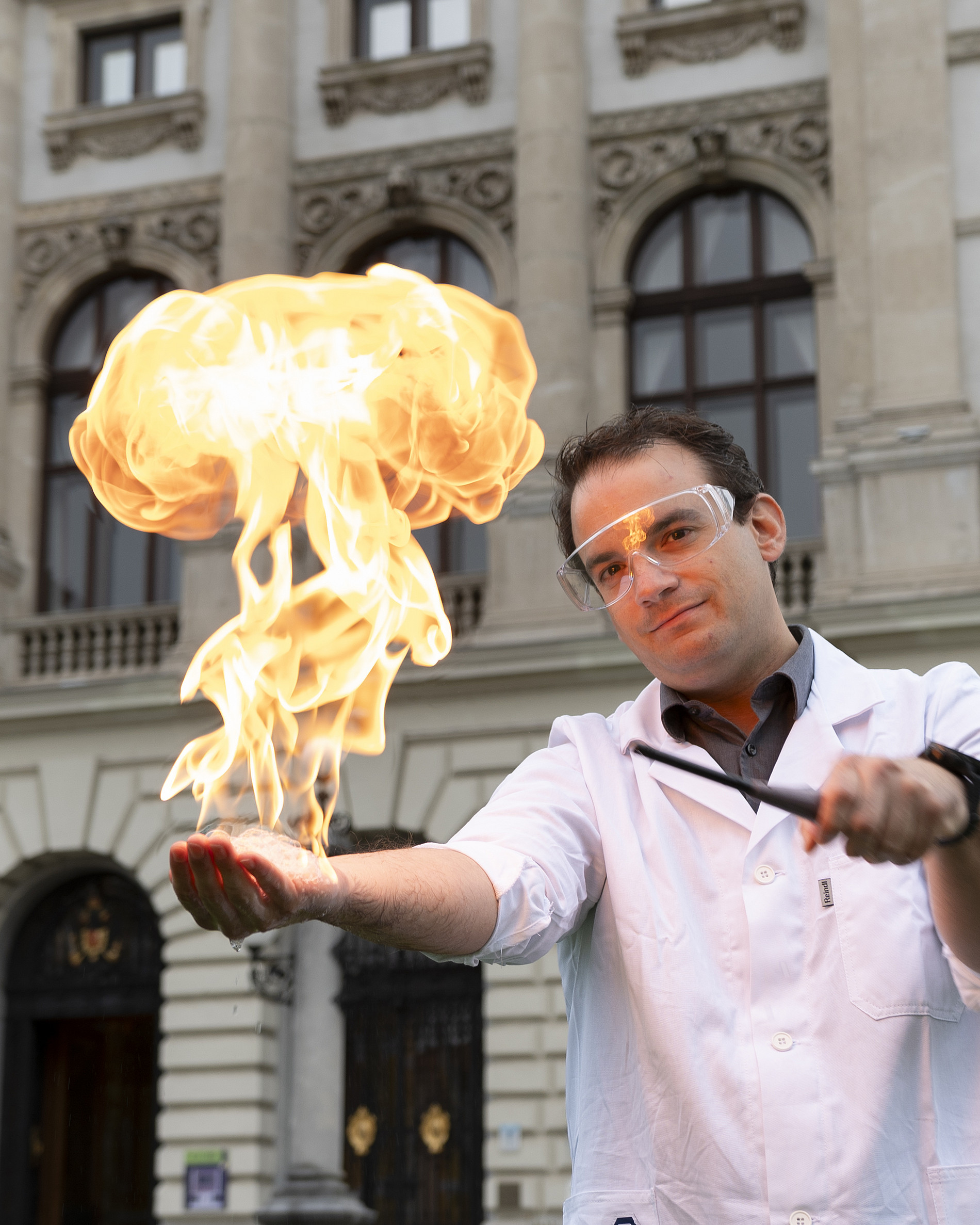 Chemiker hält Flamme in der Hand vor dem Hauptgebäude der Uni Graz 