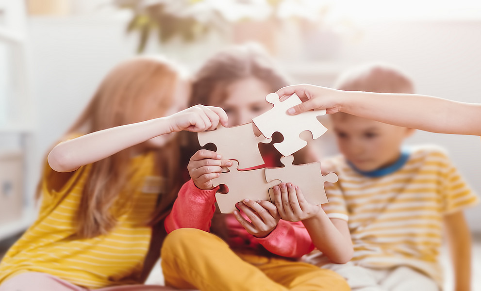 Eine Gruppe von Kindern, die zusammensitzen und Puzzleteile halten, als Symbol für Zusammenarbeit und Teamwork im Lernprozess