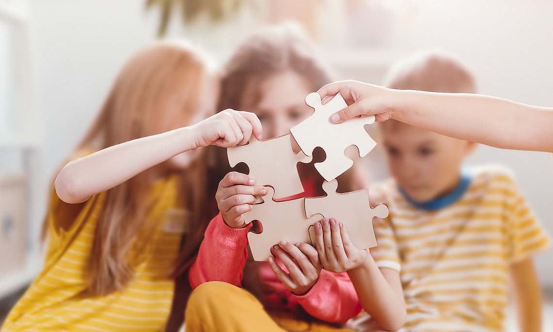 A group of children sitting together, holding puzzle pieces, symbolizing collaboration and teamwork in the learning process