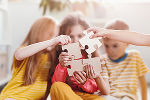 A group of children sitting together, holding puzzle pieces, symbolizing collaboration and teamwork in the learning process