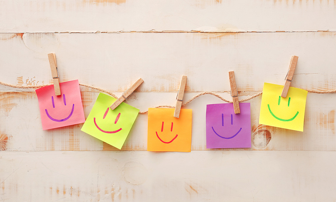  fünf Post its in verschiedenen Farben hängen auf einer Leine, auf jedem Post it befindet sich ein Smiley