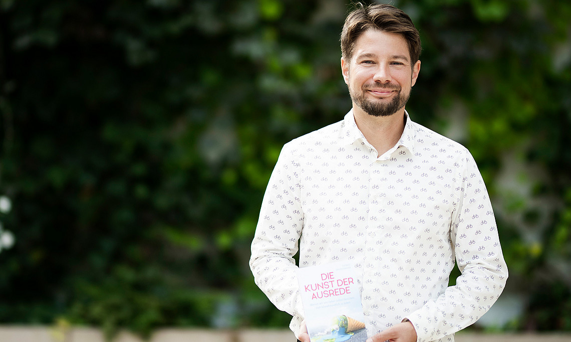Thomas Brudermann mit seinem Buch in der Hand vor einer mit Efeu bewachsenen Wand