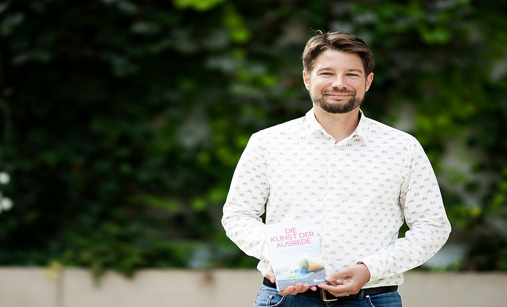 Thomas Brudermann mit seinem Buch in der Hand vor einer mit Efeu bewachsenen Wand