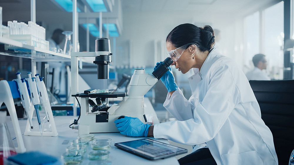 Junge Frau blickt durch ein Mikroskop in einem Labor und symbolisiert BioTechMed-Graz ©Gorodenkoff Productions OU - stock.adobe.com