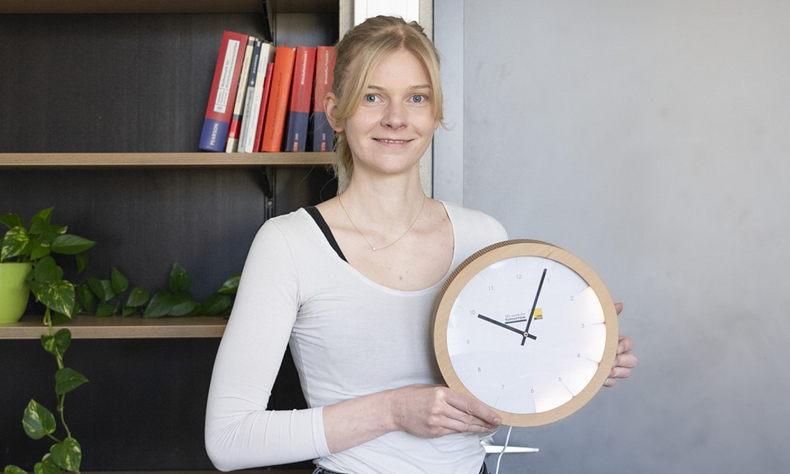 Die Forscherin hält eine Wanduhr, die im Bereich von zwei bis sechs Uhr aufleuchtet.
