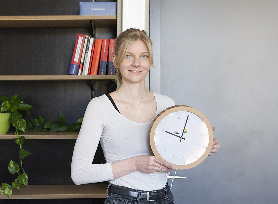 Forscherin mit einer Uhr in der Hand vor einem Bücherregal ©Uni Graz/Angele