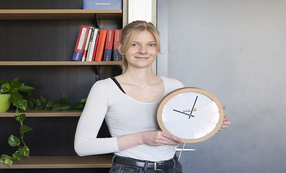 Die Forscherin hält eine Wanduhr, die im Bereich von zwei bis sechs Uhr aufleuchtet.