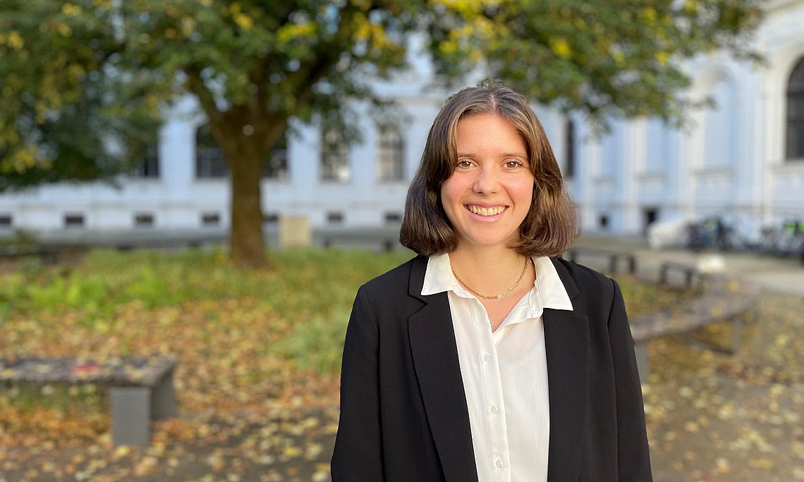Eine junge Frau steht lächelnd vor einem historischen Gebäude