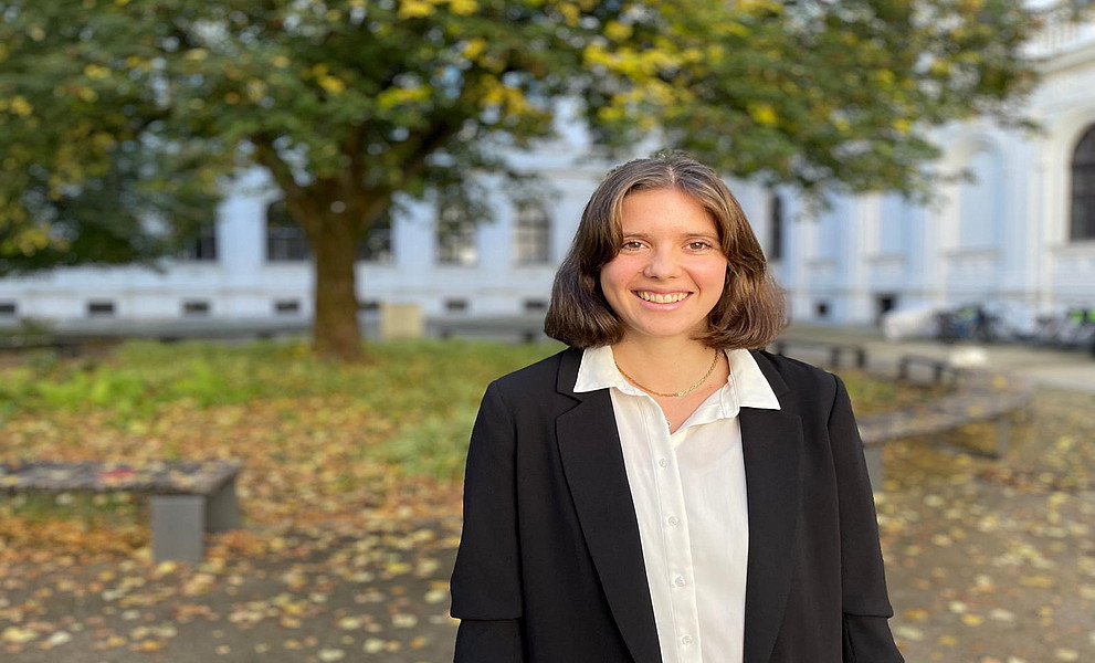 Eine junge Frau steht lächelnd vor einem historischen Gebäude