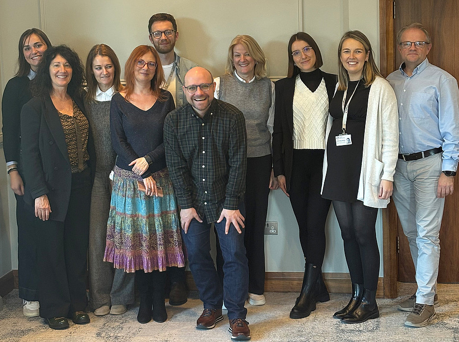 eine Gruppe aus 7 Frauen und 3 Männern, die vor einer Wand stehen und in die Kamera lächeln 