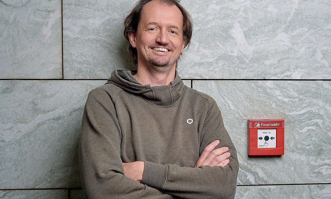 Thomas Gölles lehnt an einer Mauer, daneben ein Alarmknopff