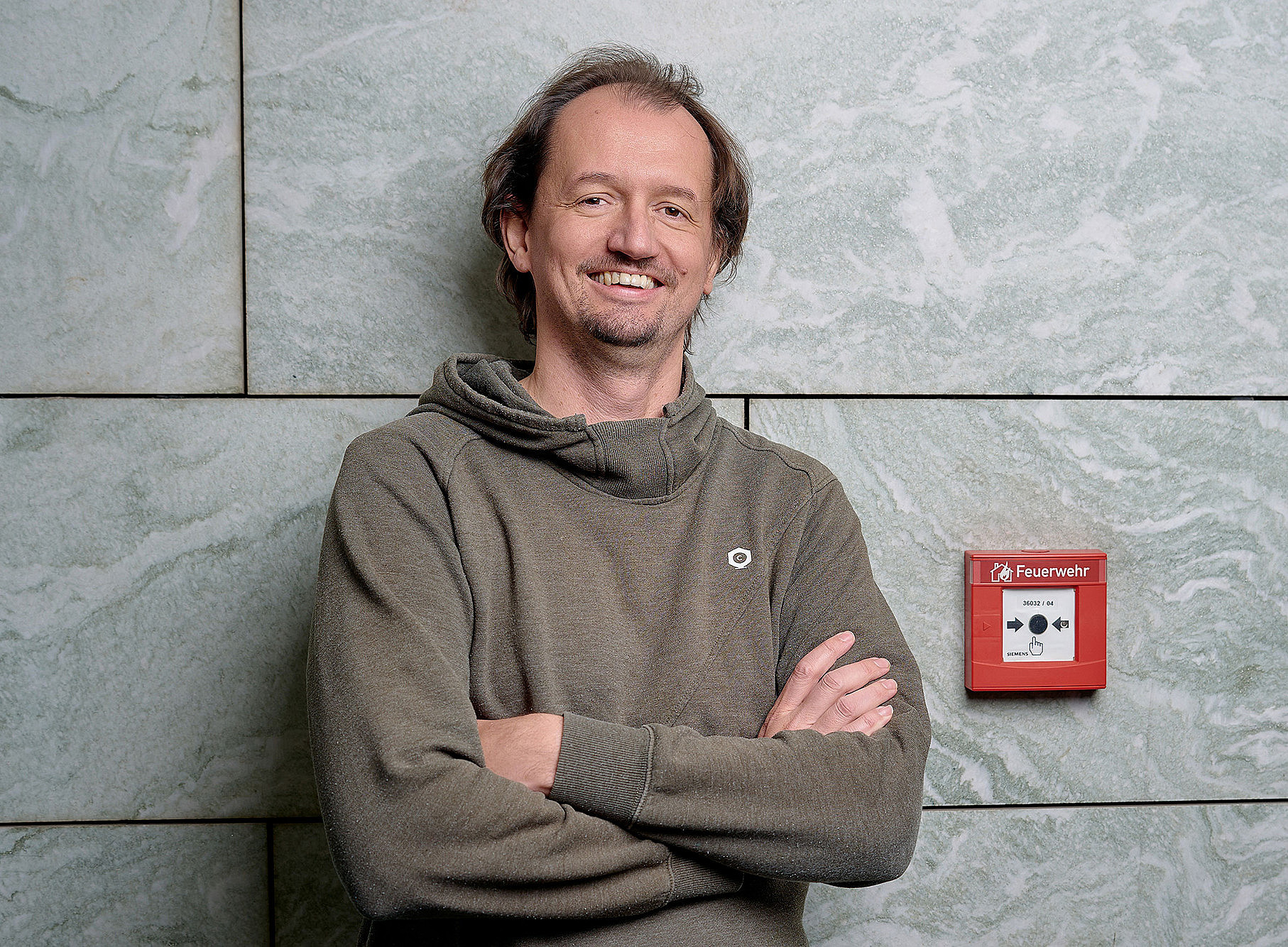 Thomas Gölles lehnt an einer Mauer, daneben ein Alarmknopff 