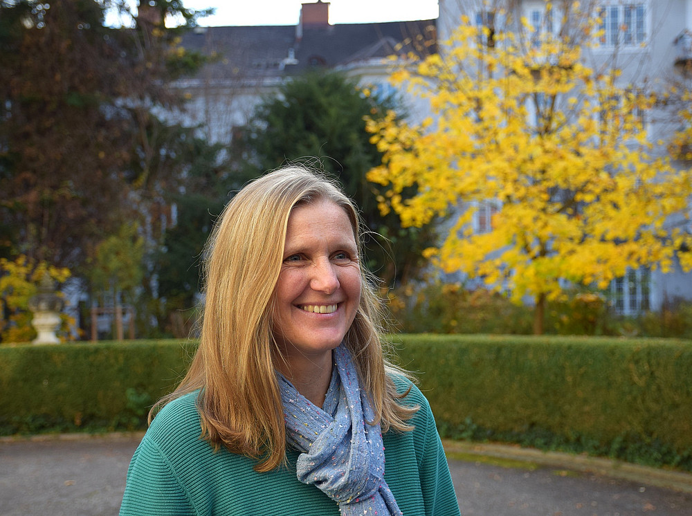 Portrait of Verena Sailer in the garden of the Meerscheinschlössl. It is autumn, she is wearing a jumper with a scarf, in the background is an autumn-coloured tree ©Ulrike Freitag, Uni Graz