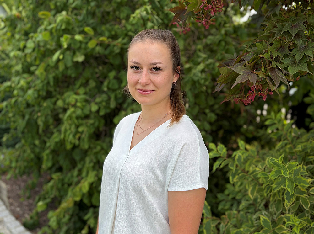 Maria Hermann steht vor einer grünen Hecke 
