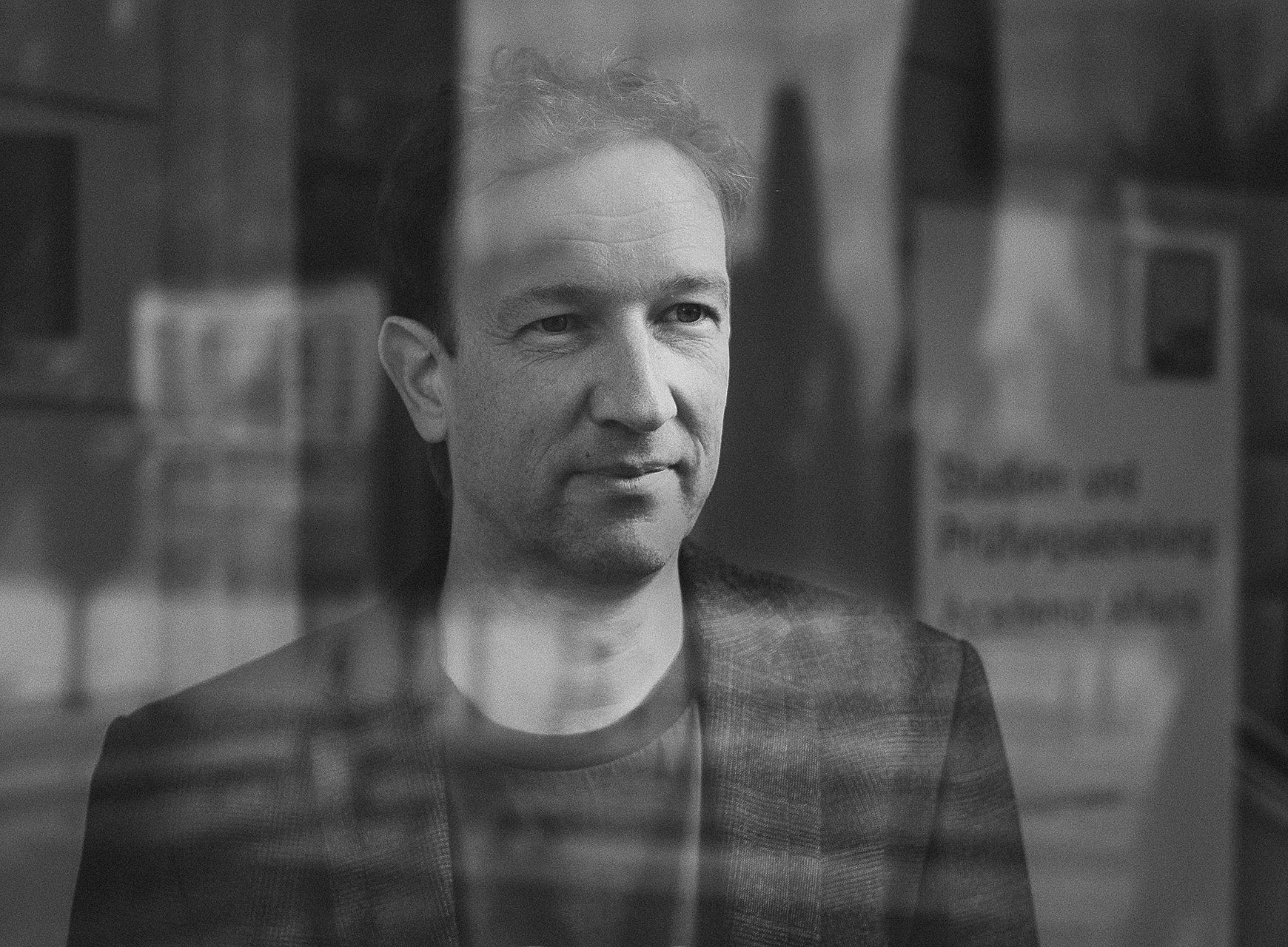 Philosoph Patrick Schuchter im Portrait durch eine Scheibe mit Spiegelungen aufgenommen ©Manuel Schaffernak