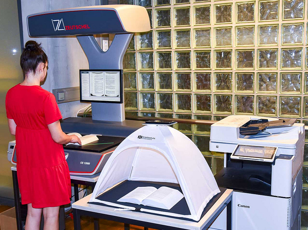 A user operates a book scanner - scan tent and multifunction copier can also be seen. ©Uni Graz/Schwarz