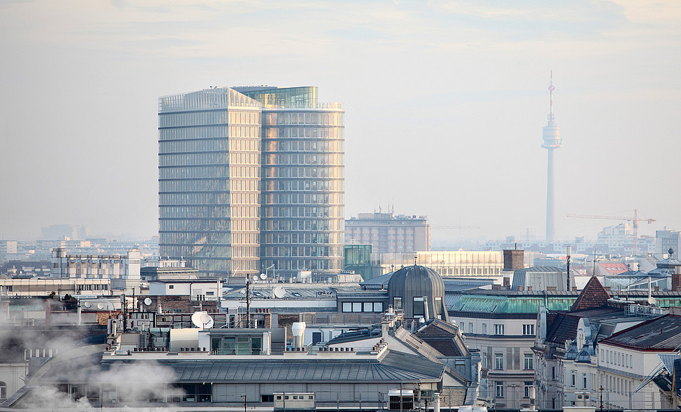 Blick von oben auf Wien mit dem UNIQA Tower und dem Donauturm, Dunst in der Luft, im Vordergrund etwas Rauch