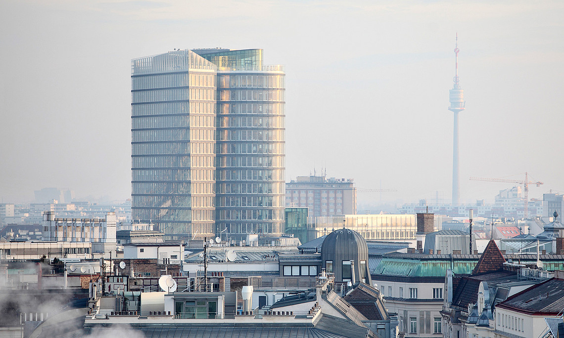 Blick von oben auf Wien mit dem UNIQA Tower und dem Donauturm, Dunst in der Luft, im Vordergrund etwas Rauch