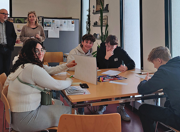 Schüler:innen sitzen um einen Tisch und lachen in die Kamera 