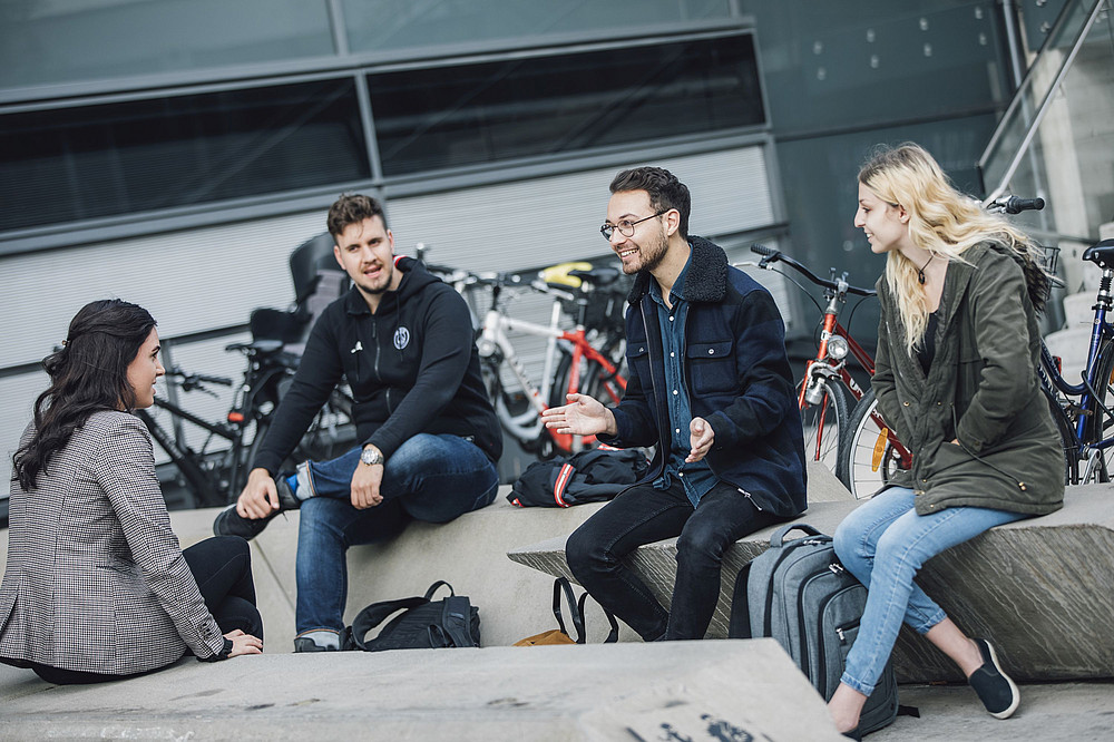 Students sit in front of the university building ©Uni Graz/Kanizaj