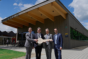 Hans-Peter Weiss, Martin Polaschek, Peter Riedler und Sebastian Ruin stehen vor dem neuen Gebäude mit einem Holzschlüssel in der Hand