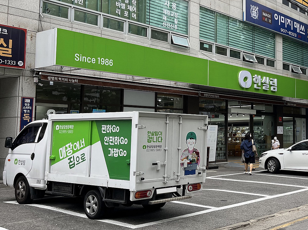 Ein kleiner grüner LKW steht vor einem koreanischen Lebensmittelgeschäft - beide gehören zu Hansalim ©JDolley