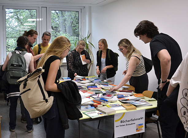 eine Gruppe Studierender steht um einen Tisch voller Bücher und schmökert ©Uni Graz/Braunegger
