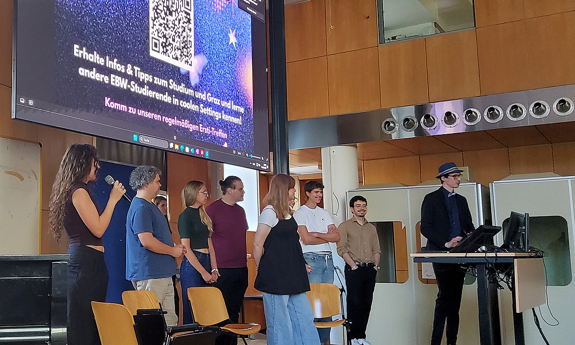 9 Studierende stehen auf einer Bühne und halten eine Präsentation