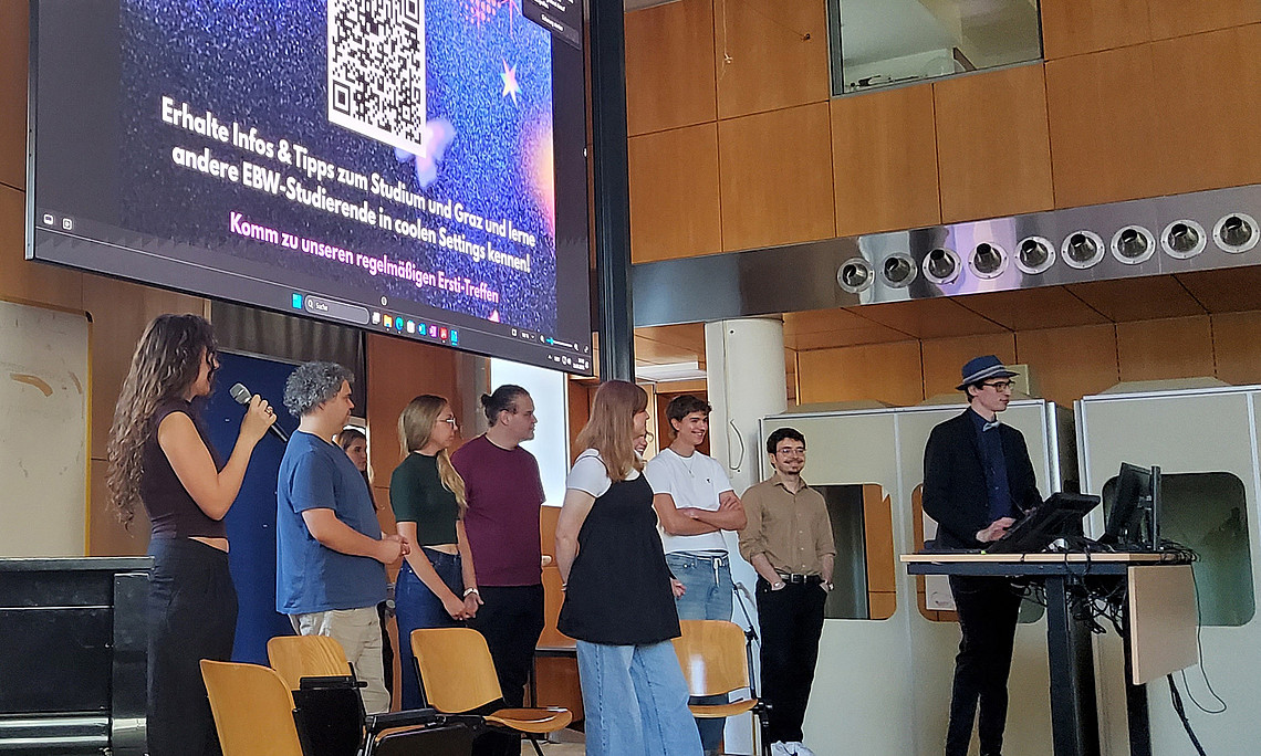 9 Studierende stehen auf einer Bühne und halten eine Präsentation