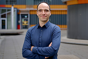 Sebastian Preissl with arms crossed, chest portrait, in the background the Centre for Molecular Biosciences at the University of Graz