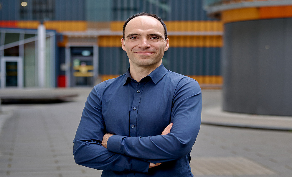 Sebastian Preissl mit verschränkten Armen, Brustbild, im Hintergrund das Zentrum für Molekulare Biowissenschaften der Uni Graz