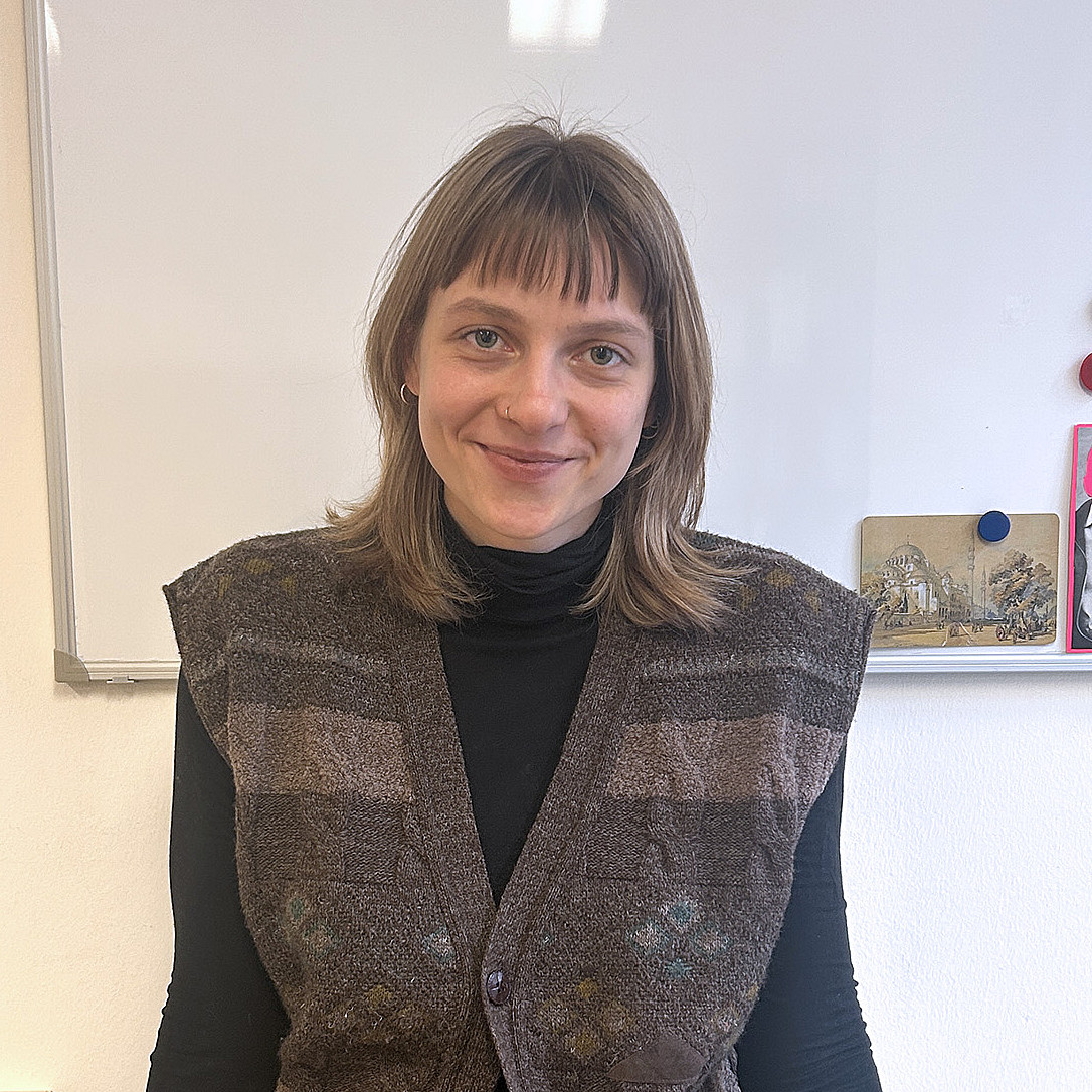 Portrait einer jungen Frau mit schulterlangen hellbraunen Haaren vor einer weißen Tafel