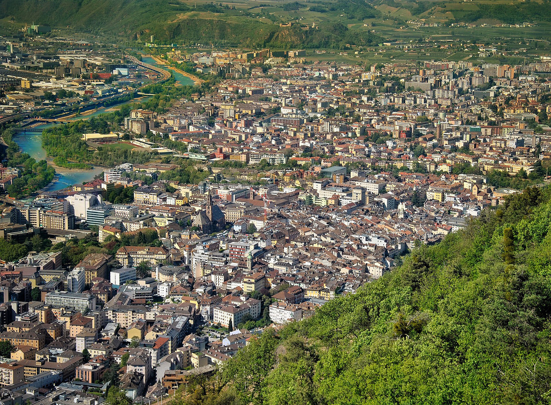 Ein Teil von Bozen von oben fotografiert. Rechts im Vordergrund ist bewaldeter Hügel, dahinter und nebenan erstreckt sich die Stadt Bozen. Links im Bild ist ein Fluss zu sehen, der sich durch die Stadt schlängelt. ©Pixabay