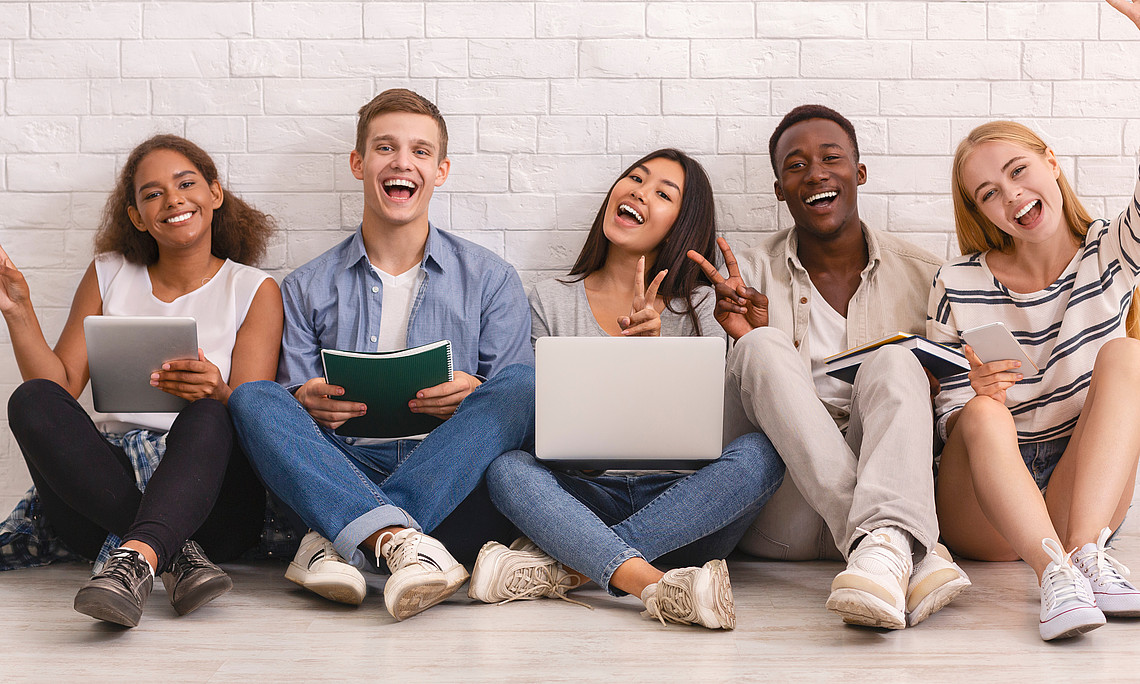 group of happy multiracial students studying for university exams, cheerfully gesturing at camera, white brick wall background