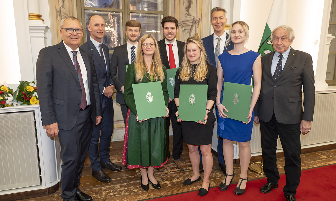 Eine Gruppe von fünf Menschen, vier Personen in der Mitte halten Urkunden. 
