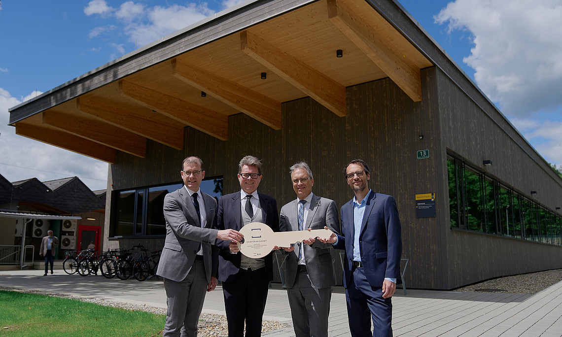 Hans-Peter Weiss, Martin Polaschek, Peter Riedler und Sebastian Ruin stehen vor dem neuen Gebäude mit einem Holzschlüssel in der Hand
