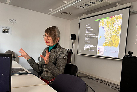 A woman sitting in front of a latop, presenting, with the big screen in the background ©Ben Gidley