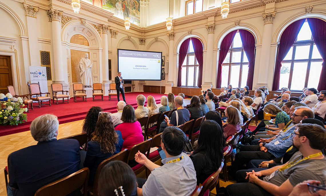 A photograph of an international scientific conference held in a 19th-century building. Speakers and audience members are listening intently during the opening ceremony.