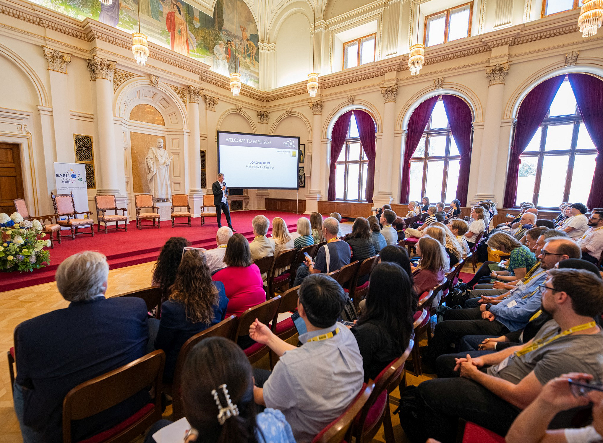 Ein Foto einer internationalen wissenschaftlichen Konferenz in einem Gebäude aus dem 19. Jahrhundert. Die Redner und Zuhörer hören während der Eröffnungszeremonie aufmerksam zu. ©Uni Graz/Tzivanopoulos