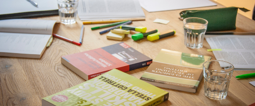 Bücher, Zettel, Stifte und Gläser auf einem Arbeitstisch